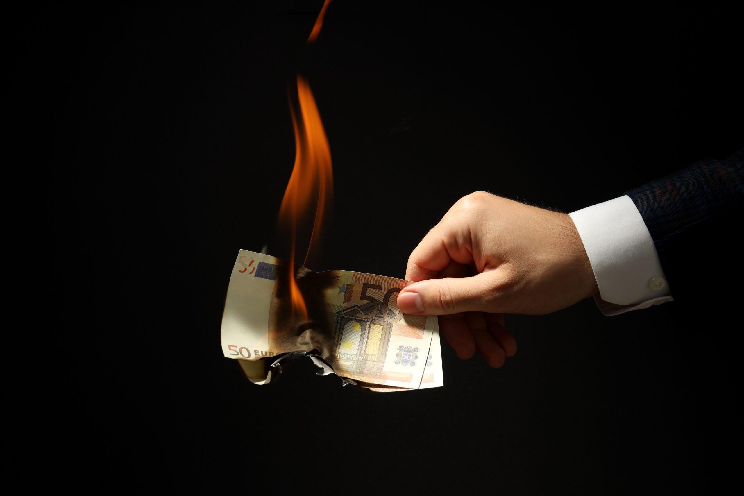 Eine Hand hält zwei brennende 50 Euro Scheine